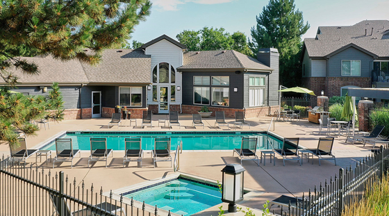 Inviting apartment complex showcasing a sparkling swimming pool, relaxing lounge chairs, and lush greenery under a bright blue sky.