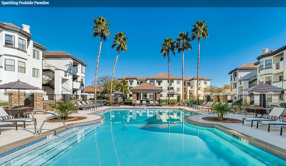 Luxury apartment complex with a sparkling pool, surrounded by palm trees and stylish sun loungers under the clear blue sky.