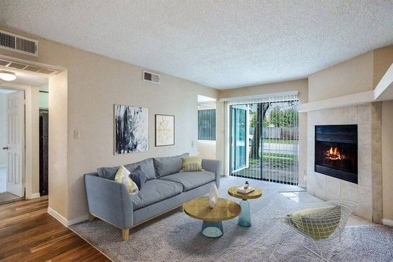 Living room with wood floors, gray rug, blue couch, circular coffee table, white brick fireplace, and a glass patio door