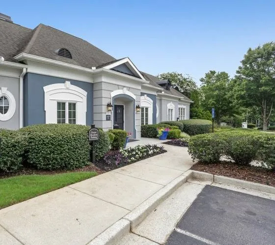 Gray and blue brick leasing office with sidewalk, parking, and landscaping