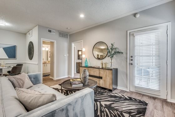 Modern living room with wood floors, patterned rug, white and gray couch, and glass patio door.