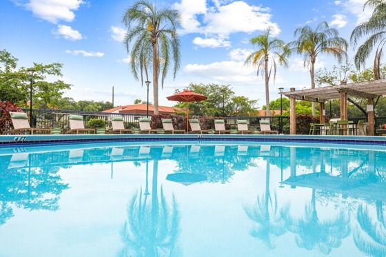 Resort-style pool with palm trees, orange umbrellas, lounge chairs, and native landscaping.