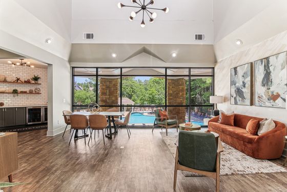 Spacious leasing office with wood floors, orange couch, chandelier, and floor-to-ceiling windows overlooking the pool and trees.