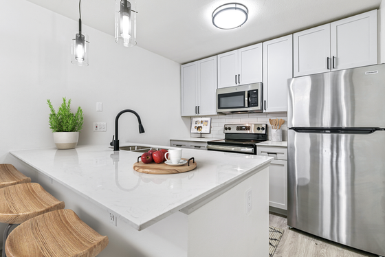 Modern kitchen with hardwood floors, white quartz island, stainless steel appliances, and white cabinetry
