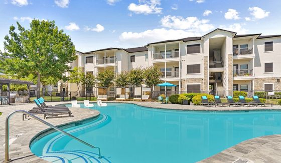 Luxurious apartment complex featuring a sparkling resort-style pool, surrounded by stylish loungers and lush greenery, ideal for relaxation.
