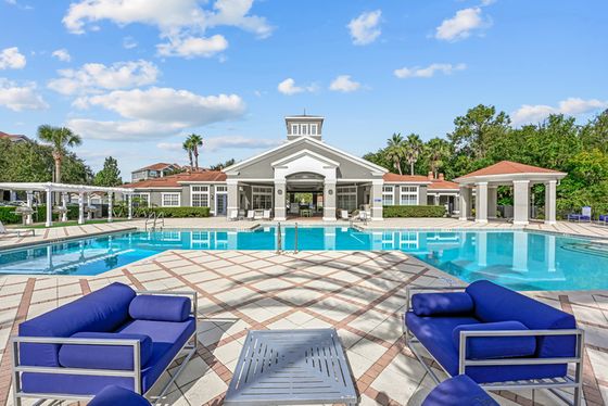 Swimming pool with expansive deck, modern lounge chairs, and leasing office in the background under a bright blue sky.