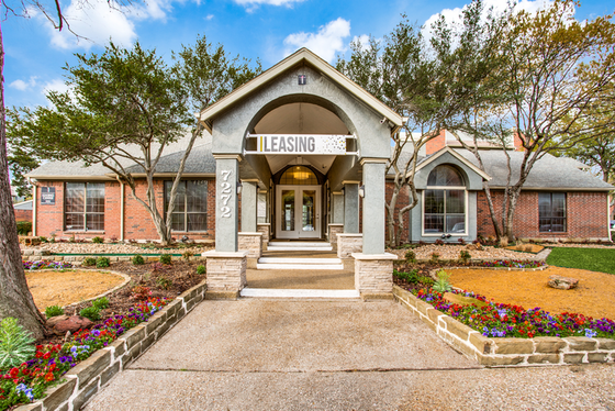 Inviting leasing office with charming brick facade, elegant landscaping, and welcoming entrance set against a clear blue sky.