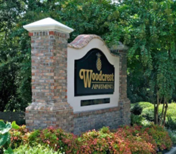 Welcoming entrance sign for Woodcrest Apartments, surrounded by lush greenery and vibrant flowers.