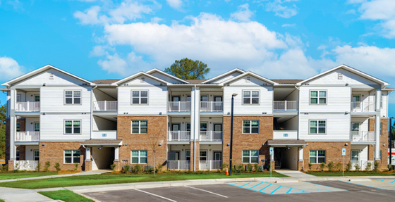 Charming three-story apartment building with modern brick and white siding, surrounded by well-maintained greenery, offering inviting balconies and ample parking.