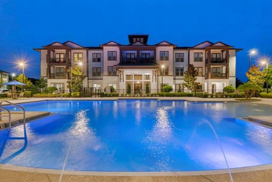Night view of pool with fountains facing apartment community