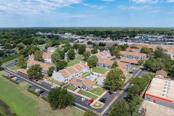 Aerial view of a charming residential community featuring lush green spaces, modern buildings with red roofs, and a central swimming pool.