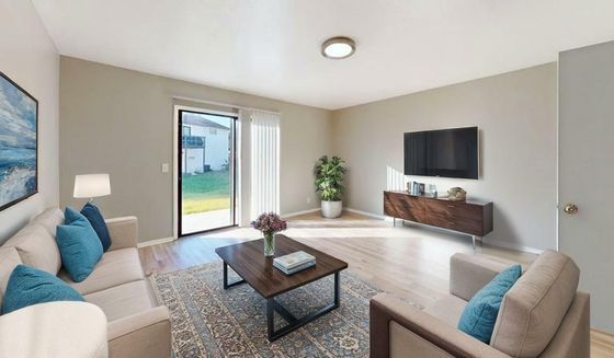 Inviting living room with a cozy beige sofa, vibrant blue cushions, and sliding glass doors opening to a lush outdoor view. Features a stylish coffee table, decorative rug, and a sleek wall-mounted TV creating a spacious and modern ambiance.