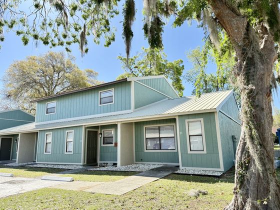 Charming duplex with a fresh green exterior, nestled under mature trees, offering a serene suburban vibe.
