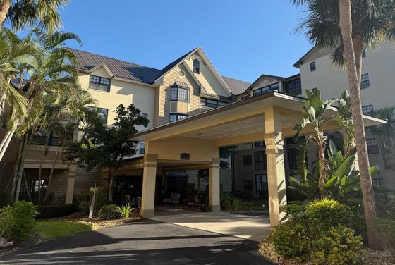 Charming multi-story apartment building with tropical landscaping and welcoming front entry on a bright sunny day.