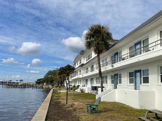Charming waterfront apartment building with palm trees, offering serene views and ample outdoor seating.