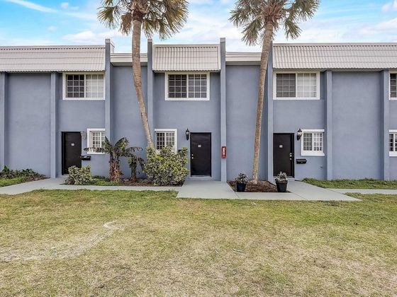 Inviting townhouse exterior with modern design, surrounded by lush greenery and tropical palm trees.
