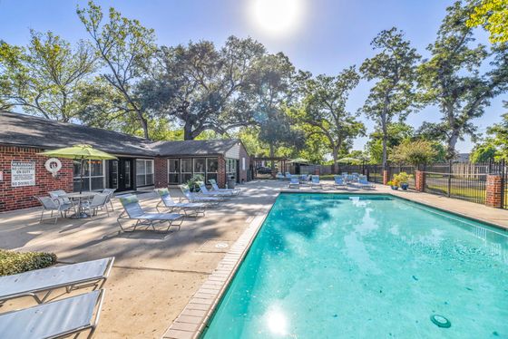 Inviting outdoor pool area with comfortable lounge chairs, surrounded by lush greenery and a charming brick building, perfect for relaxation and leisure.