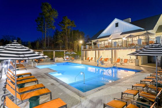 Luxurious outdoor swimming pool at night with stylish lounge chairs and a modern clubhouse.