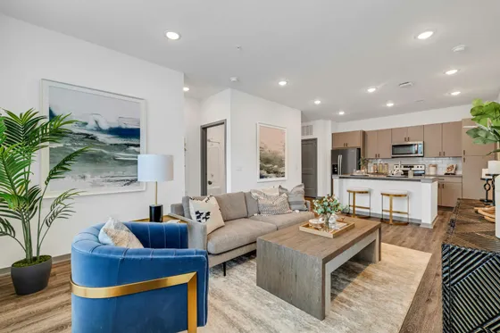 Contemporary open-plan living space with elegant furnishings, featuring a stylish blue accent chair, cozy gray sofa, and sleek kitchen with modern appliances.