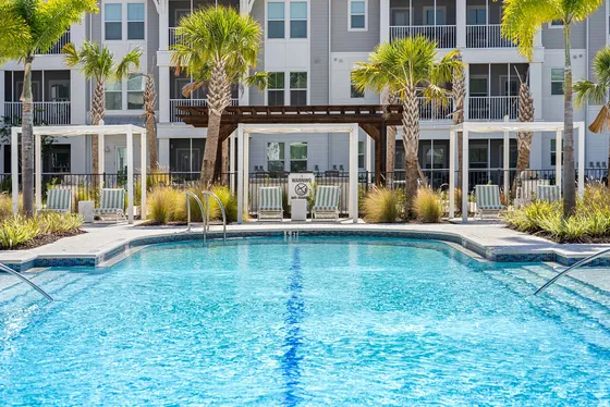 Luxurious apartment complex featuring a sparkling swimming pool surrounded by elegant palm trees and sun loungers, offering a tropical oasis for residents.