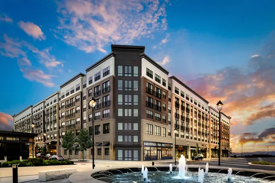 Elegant multi-story apartment building with modern design, surrounded by beautifully landscaped grounds and a charming fountain at sunset.