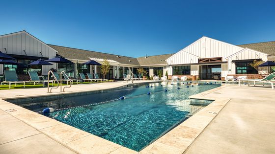 Inviting outdoor pool area with sun loungers, modern clubhouse, and vibrant umbrellas under a clear blue sky.