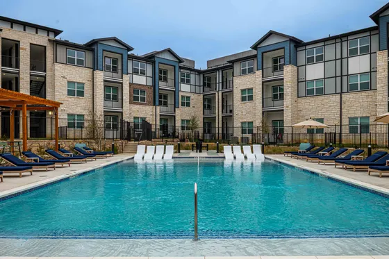 Elegant apartment complex with a sparkling pool, luxurious loungers, and contemporary architecture.