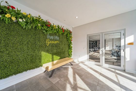 Inviting fitness center entrance with lush green wall and vibrant flowers, featuring a motivational 'live life' sign and a stylish bench.