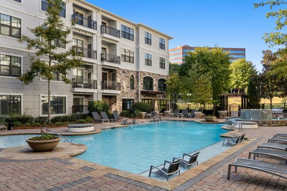 Modern apartment building with a beautiful outdoor pool, surrounded by lounge chairs and lush landscaping.