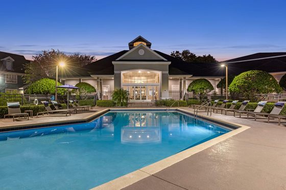 Elegant outdoor pool area with lounge chairs and lush greenery under twinkling evening lights.