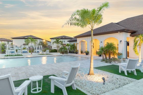 Luxurious outdoor pool area with elegant lounge chairs, palm trees, and a stylish clubhouse at sunset.