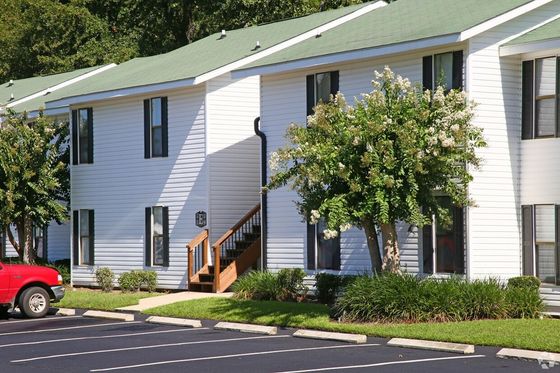 Charming white apartment building with green roofs, surrounded by lush greenery and ample parking.