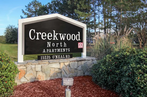 Welcoming sign at Creekwood North Apartments surrounded by lush greenery and trees.