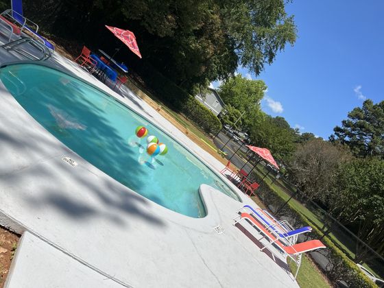 Inviting outdoor pool area with colorful beach balls and stylish lounge chairs, surrounded by lush greenery.