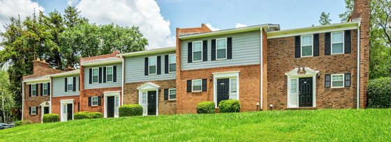 Charming brick-front townhouses with black shutters, nestled in a lush green landscape under a clear blue sky.