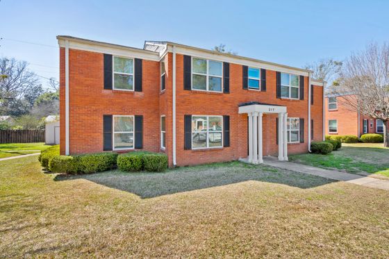 Charming red brick apartment building with classic black shutters and well-maintained landscaping in a serene neighborhood setting.