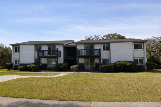 Beautifully maintained two-story apartment building with charming balconies and neatly trimmed shrubbery, set against a serene blue sky backdrop.