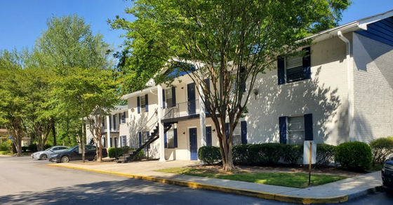 Charming two-story apartment complex with modern white facade, nestled among lush trees with convenient parking.