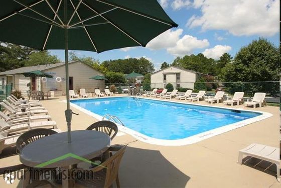Inviting residential pool area with ample seating and umbrellas, surrounded by lush greenery and vibrant blue skies.
