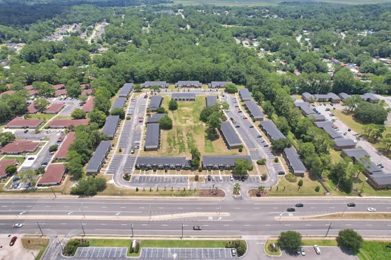 Aerial view of a well-organized apartment complex surrounded by lush greenery, showcasing ample parking and a spacious central courtyard.
