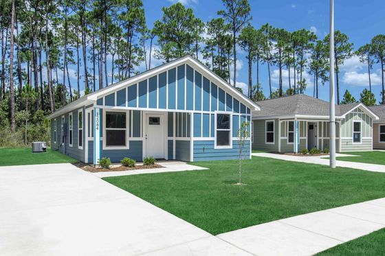 Charming blue and white cottage-style home with manicured lawn and peaceful wooded backdrop.