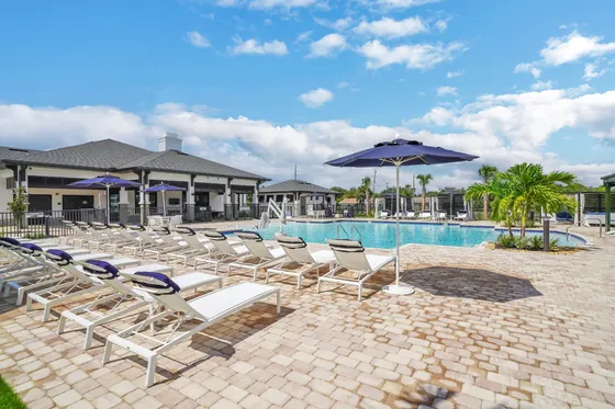 Luxurious apartment complex featuring a sparkling swimming pool with lounging chairs and umbrellas under a clear blue sky.