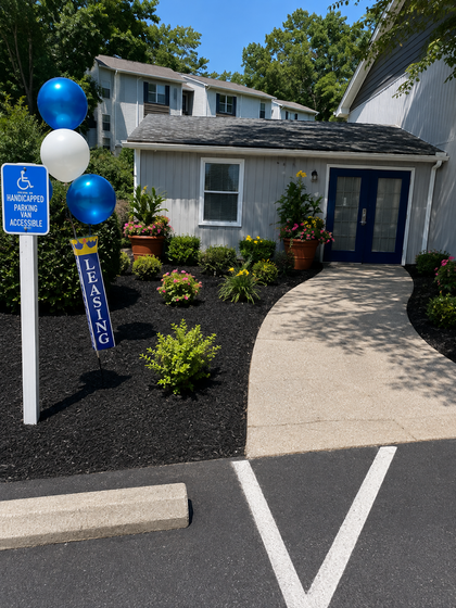 Inviting entrance to a leasing office adorned with elegant blue and white balloons, surrounded by lush landscaping and vibrant flowers, highlighting accessibility features.