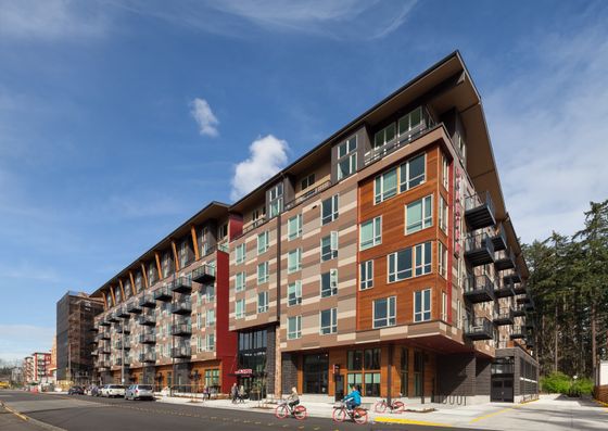 Modern, multi-story apartment building with vibrant facade, abundant windows, and street views featuring cyclists and pedestrians.