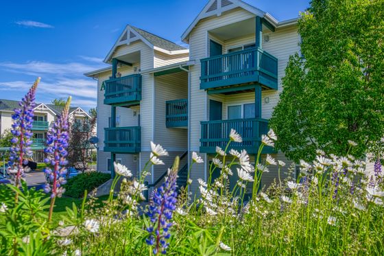 Charming apartment building with vibrant balconies and lush landscaping, nestled in a picturesque setting with blooming flowers and clear blue skies.