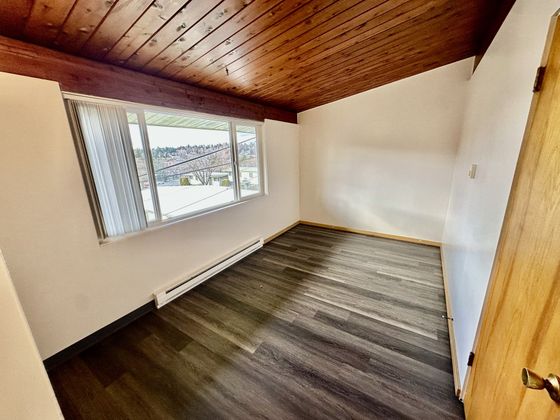 Charming room with elegant wood-paneled ceiling, large window for natural light, and sleek dark flooring, offering a cozy and inviting atmosphere.