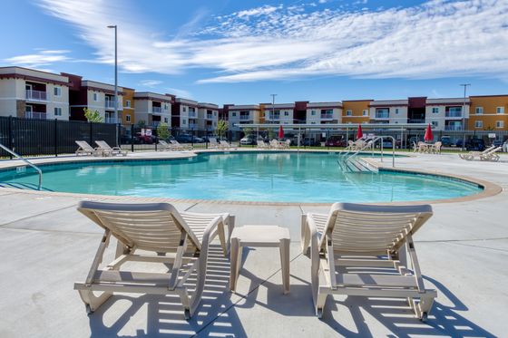 Inviting swimming pool area with sun loungers and modern apartment buildings in the background under a clear blue sky.