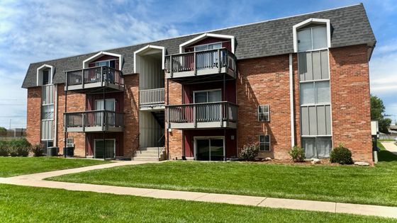Charming three-story brick apartment building with balconies and lush green landscaping under a vibrant blue sky.
