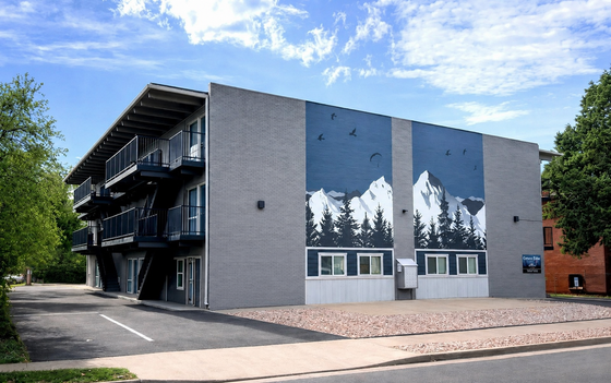 Modern apartment building featuring artistic mountain mural, with spacious balconies and lush green surroundings.