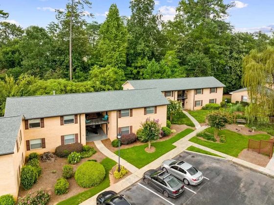 Charming apartment complex with lush greenery, showcasing ample parking and serene, well-maintained gardens.